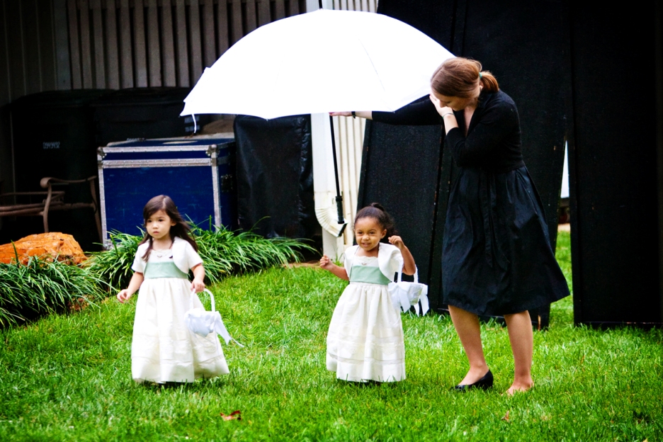 wedding planner holds umbrella over the 2 flower girls as they walk to the ceremony