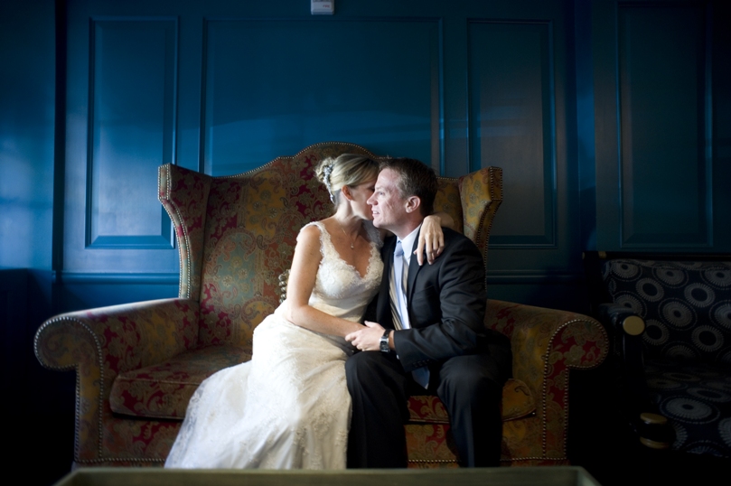 bride and groom cuddle on a love seat in the lobby of the Hotel Monaco in Alexandria VA