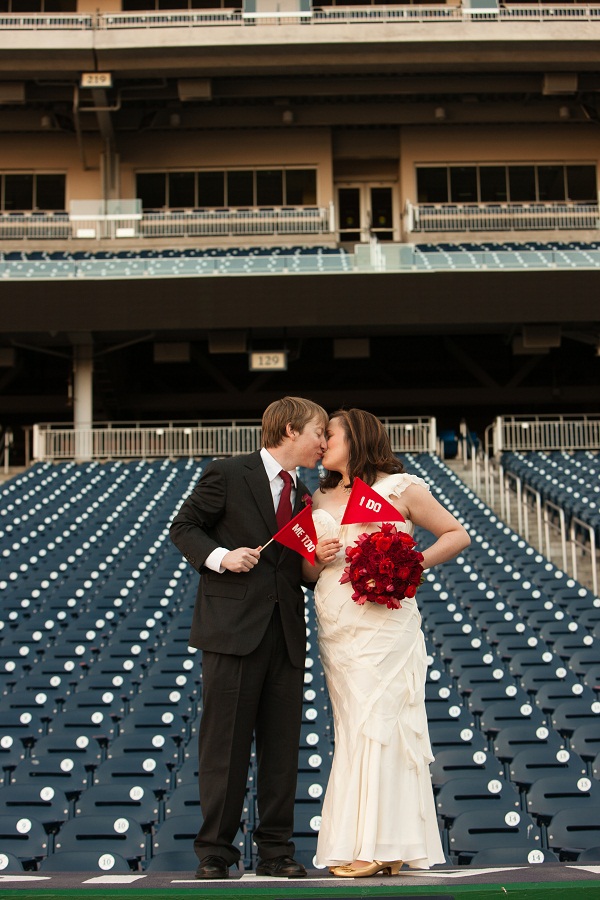 Green Event Venue in DC: Nationals Park Wedding - bride and groom stand on top of the dugout with pennant flags that say "I do" and "Me too"