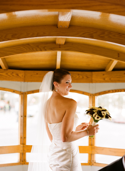 bride stands on the trolley while holding her white and purple calla lilly bouquet
