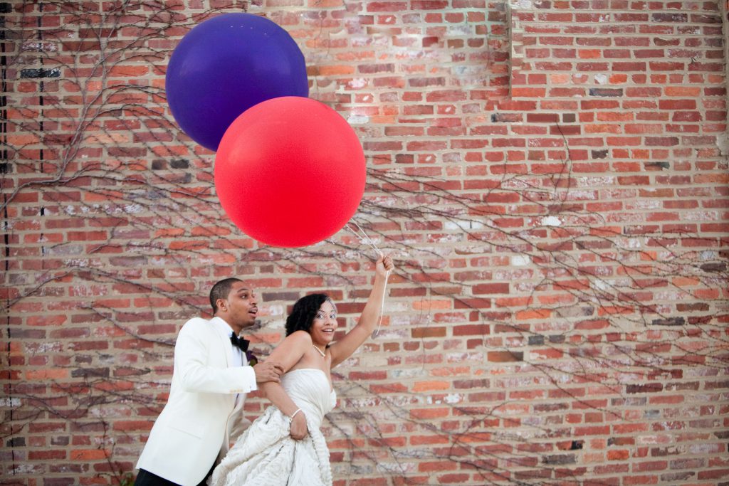 bride and groom holding red and purple big balloons
