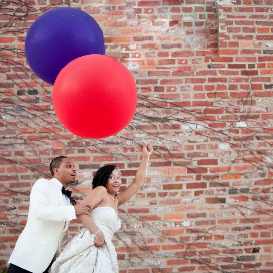 bride and groom holding red and purple big balloons