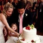 bride, groom and their daughter cut the cake
