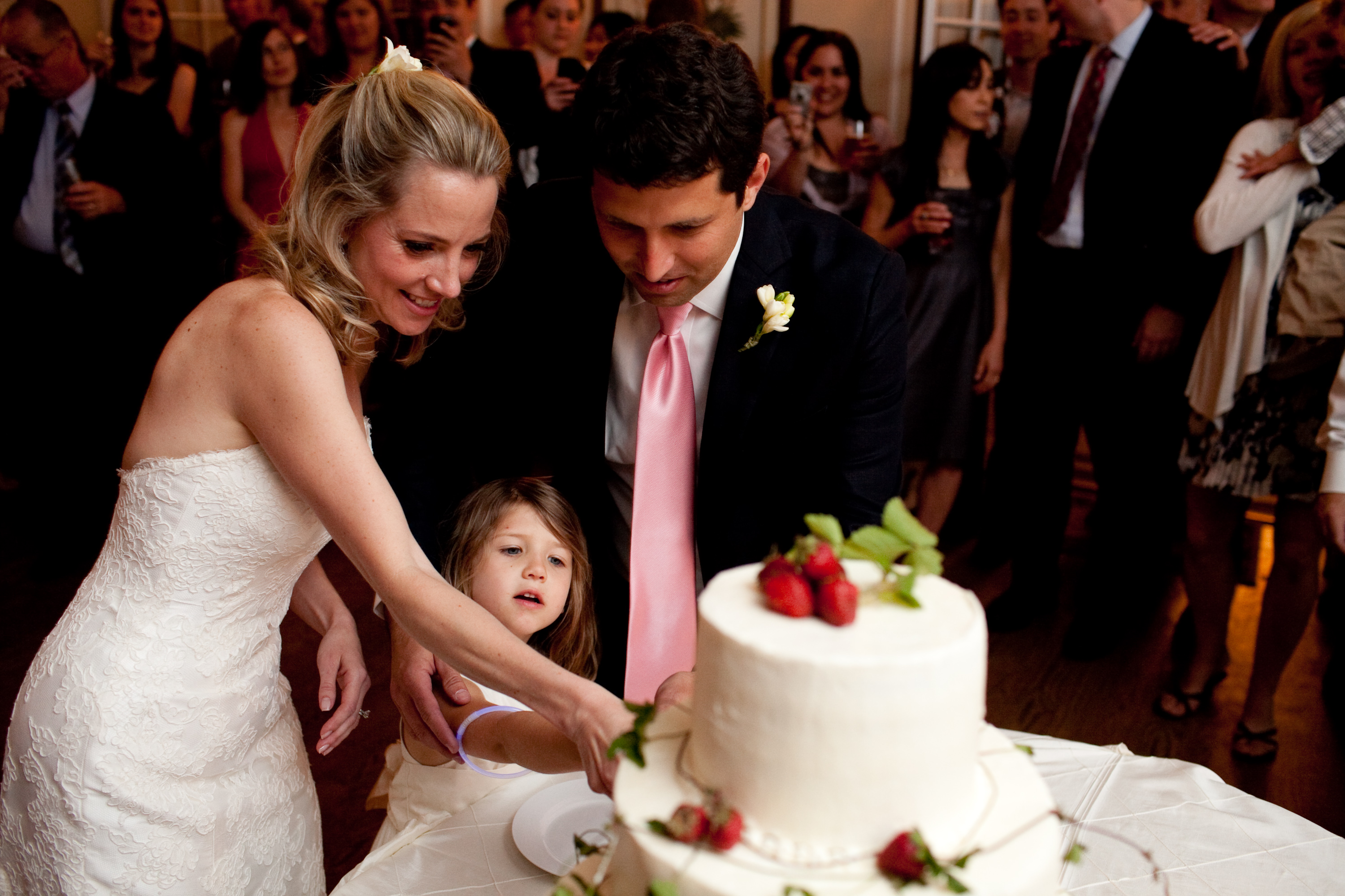 bride, groom and their daughter cut the cake