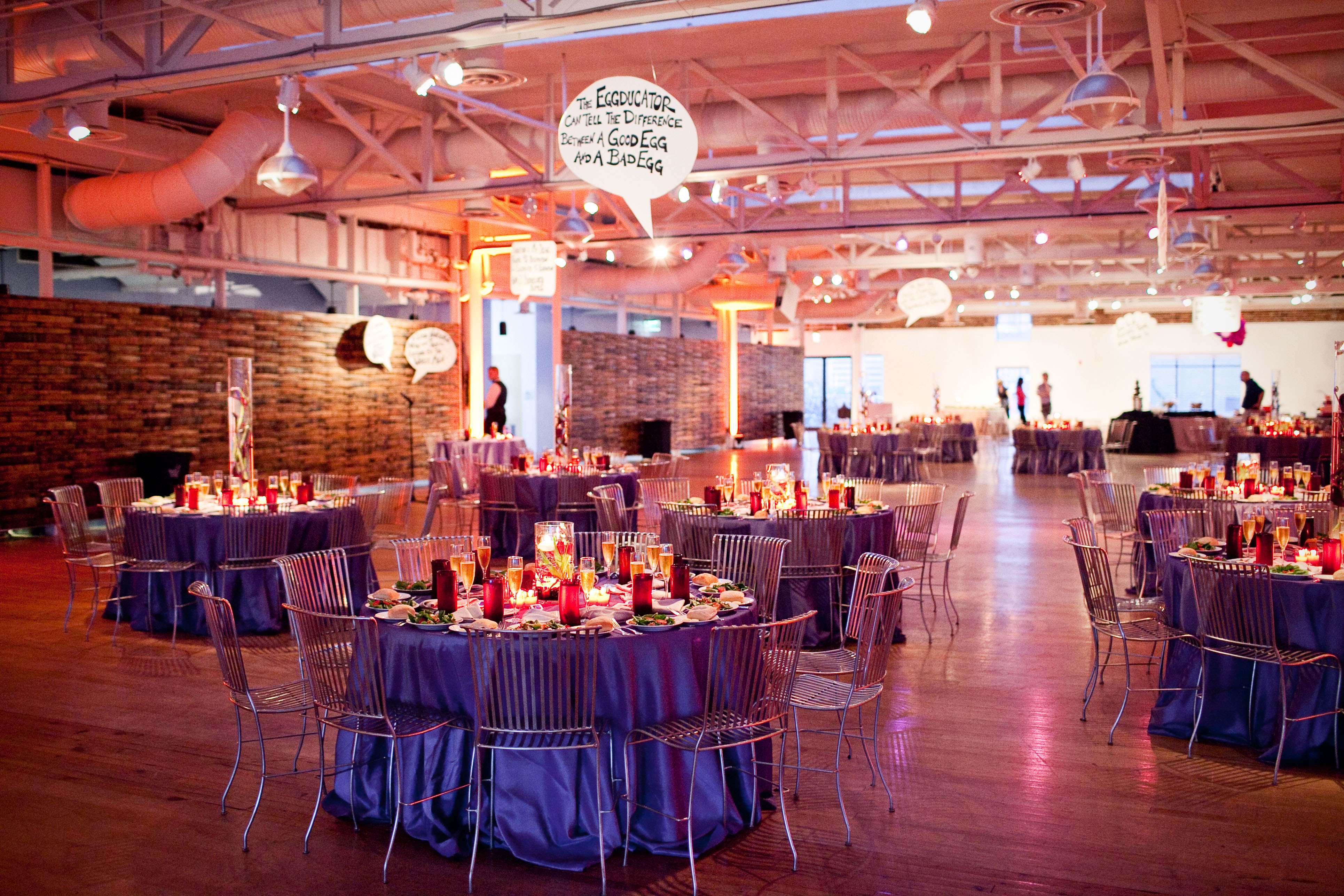 wide shot of the wedding reception with purple linens, metal chairs and overhead word bubbles featuring willy wonka quotes