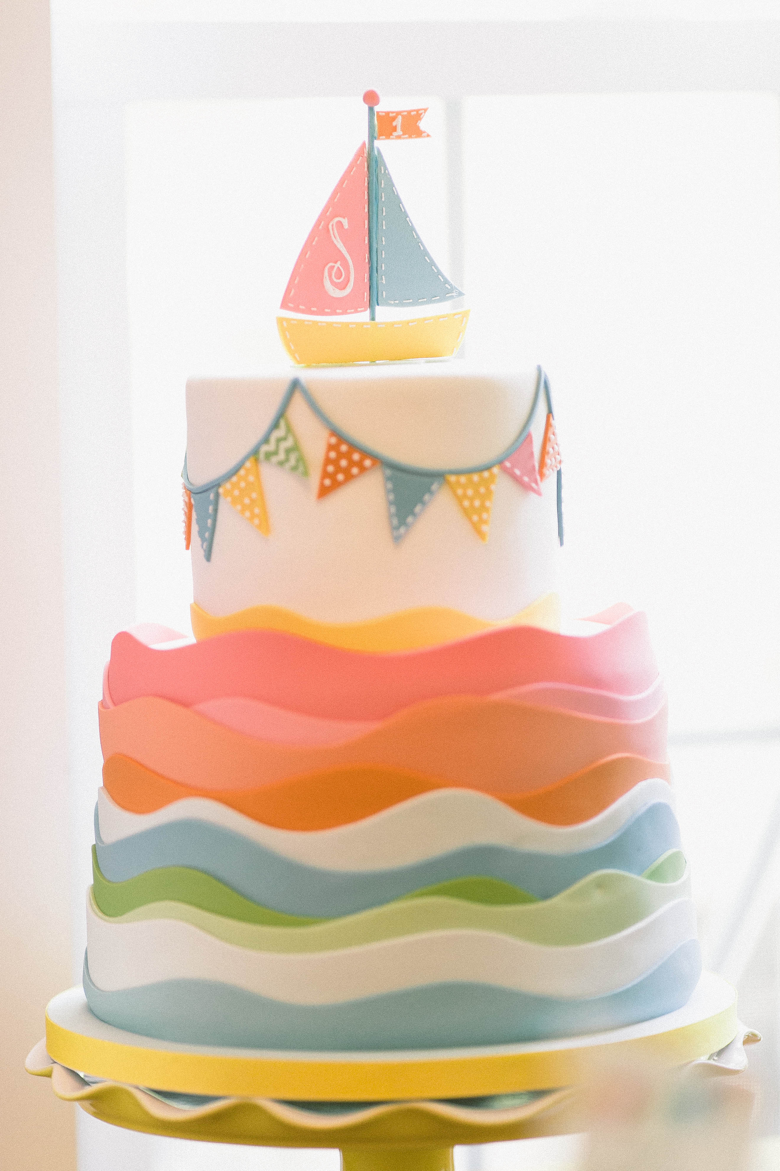colorful 2 tiered birthday cake with a sail boat on top