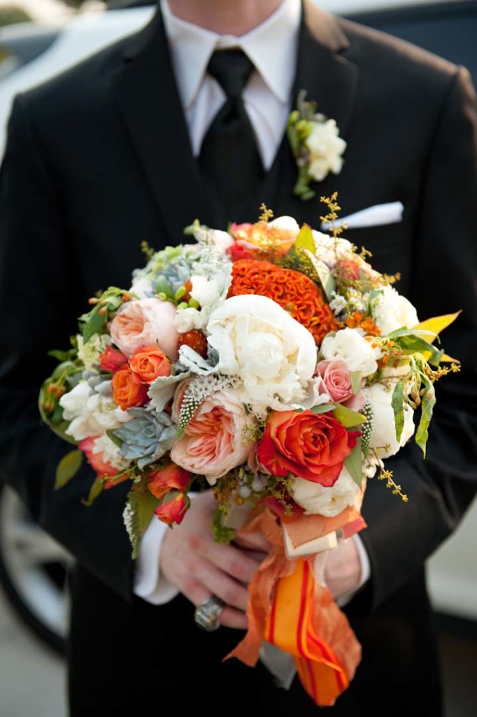 a groom holed a white and orange bridal bouquet