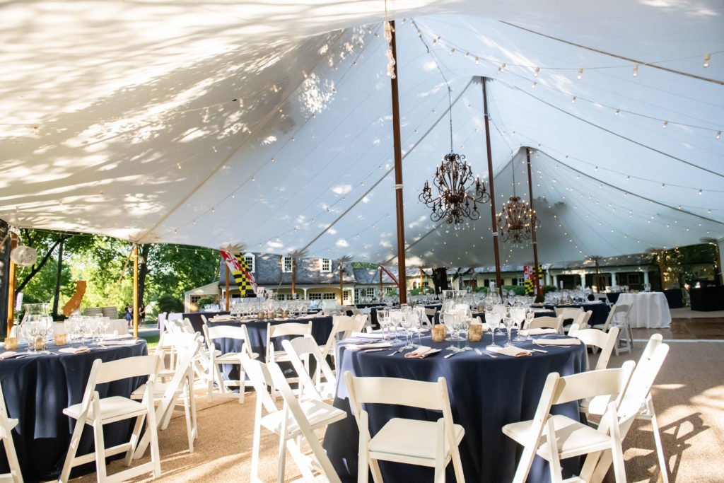 A sailcloth tent set up in a Maryland front yard for a wedding reception. White folding chairs and navy linens at round tables. coordinated by Bellwether Events 