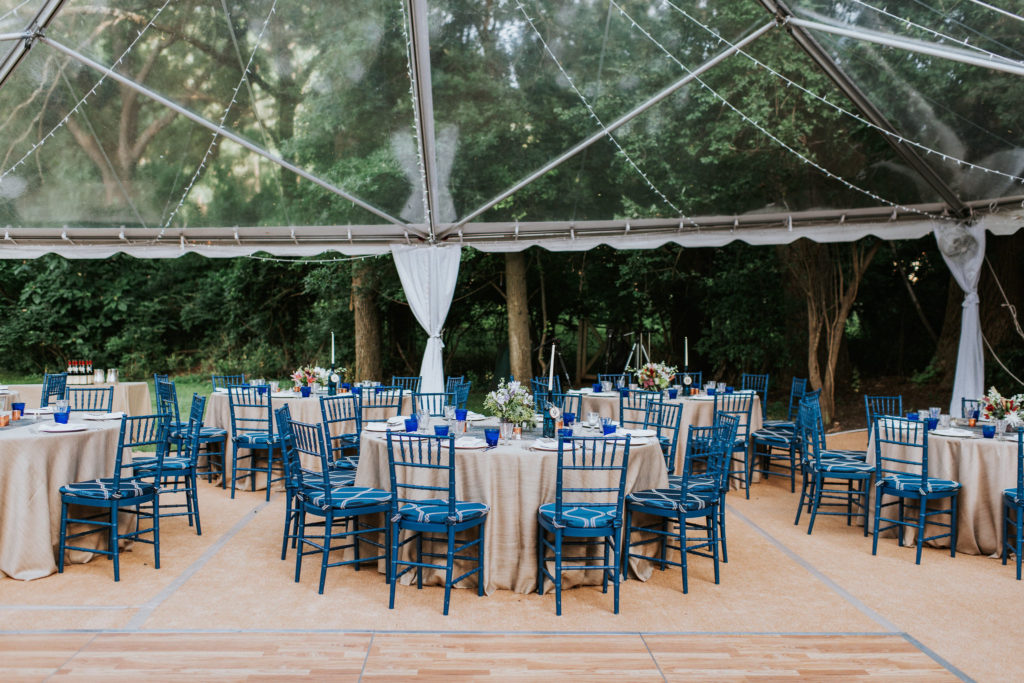 virginia home wedding reception under a clear top tent, with round dinner tables with neutral linens and cobalt blue chairs - planned by Bellwether Events
