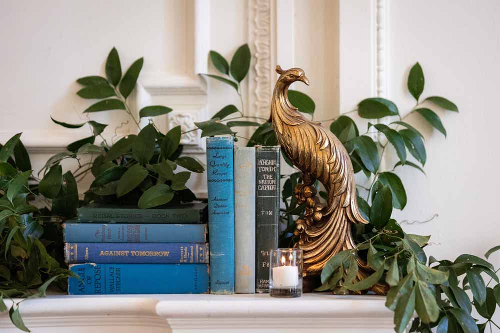 Colorful Spring DAR wedding - greenery fireplace mantel with books and brass peacocks